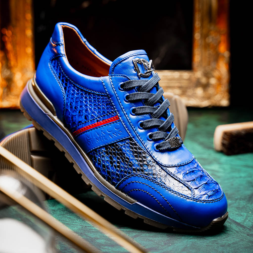 The Brescia Electric Blue sneakers by Marco Di Milano feature blue python leather, black laces, a red stripe, hand-painted side panels, and brown rubber soles—displayed with one shoe upright and the other on its side.
