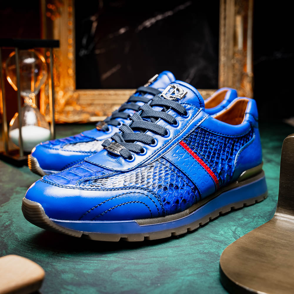 The Brescia Electric Blue sneakers by Marco Di Milano feature blue python leather, black laces, a red stripe, hand-painted side panels, and brown rubber soles—displayed with one shoe upright and the other on its side.
