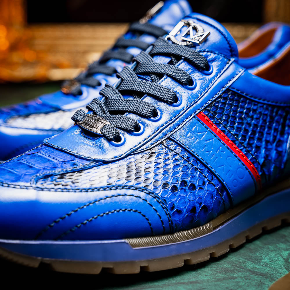 The Brescia Electric Blue sneakers by Marco Di Milano feature blue python leather, black laces, a red stripe, hand-painted side panels, and brown rubber soles—displayed with one shoe upright and the other on its side.