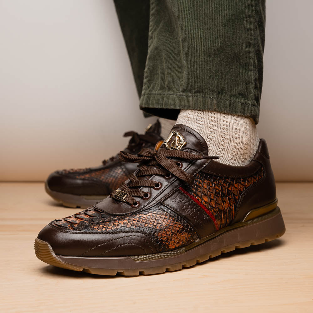 The Marco Di Milano Brescia Washed Cognac sneakers feature brown leather with a snakeskin pattern, gold accents, and rubber soles; one shoe is propped stylishly against the other, showcasing luxury footwear appeal.