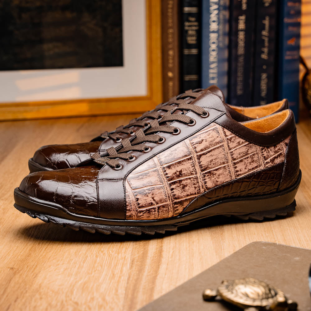 The Marco Di Milano Cairo Brown/Orix men's sneakers feature brown luxury footwear with textured panels and rubber soles, crafted to resemble genuine alligator. One shoe stands upright while the other lies on its side.