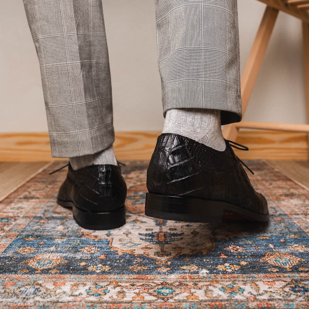 The Marco Di Milano Cancun Black features genuine hornback caiman crocodile shoes with a pointed toe, one upright and the other showing the branded brown leather sole—a striking choice in men's exotic footwear.