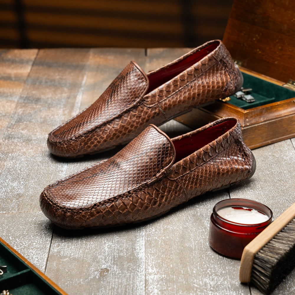 A pair of Capri Brown luxury exotic shoes by Marco Di Milano, crafted from genuine python leather, with one handcrafted men’s loafer standing upright and the other displayed on its side to highlight the intricately textured sole.