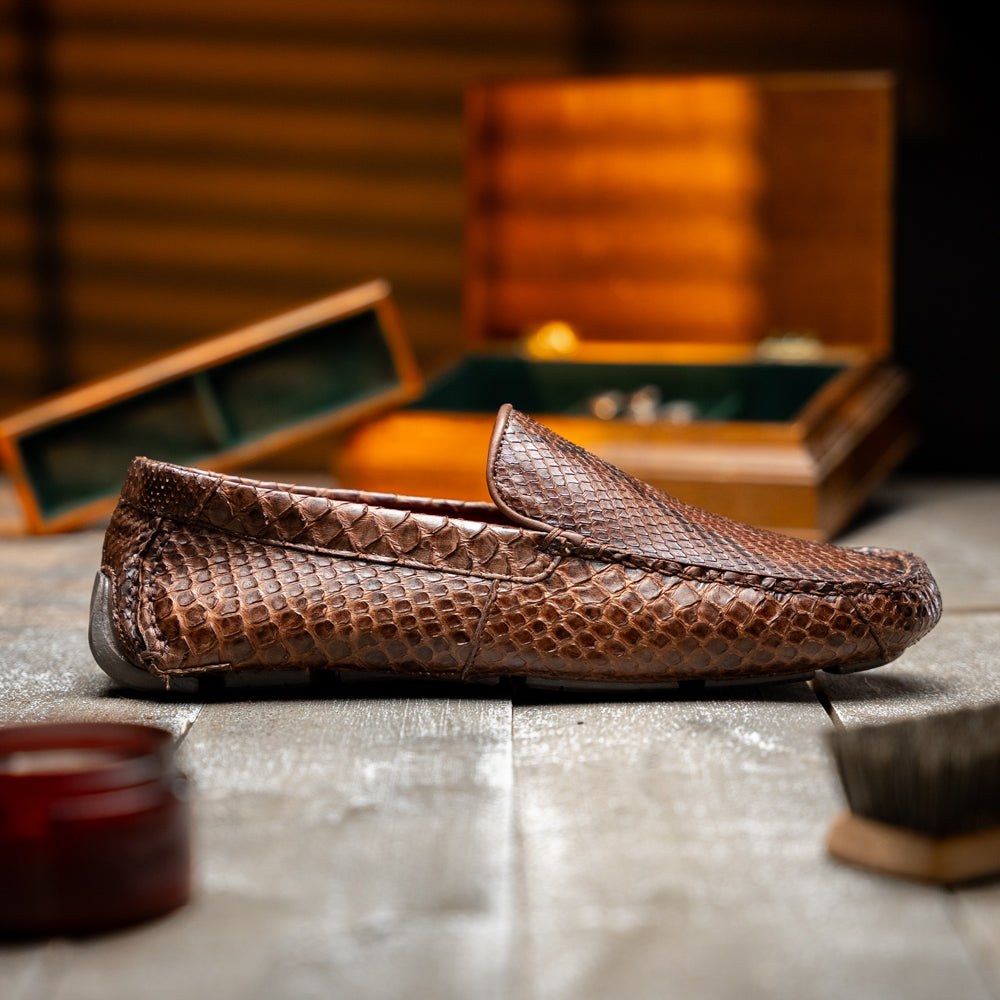 A pair of Capri Brown luxury exotic shoes by Marco Di Milano, crafted from genuine python leather, with one handcrafted men’s loafer standing upright and the other displayed on its side to highlight the intricately textured sole.