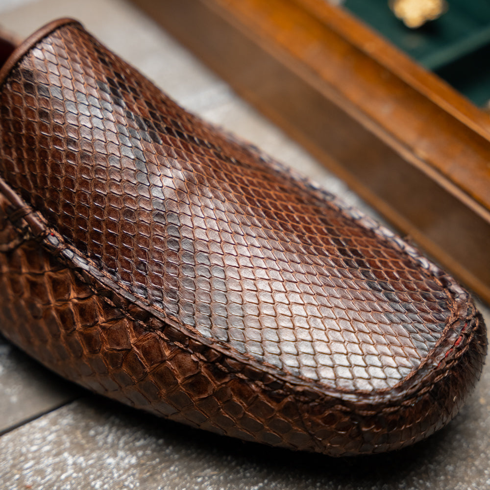 A pair of Capri Brown luxury exotic shoes by Marco Di Milano, crafted from genuine python leather, with one handcrafted men’s loafer standing upright and the other displayed on its side to highlight the intricately textured sole.