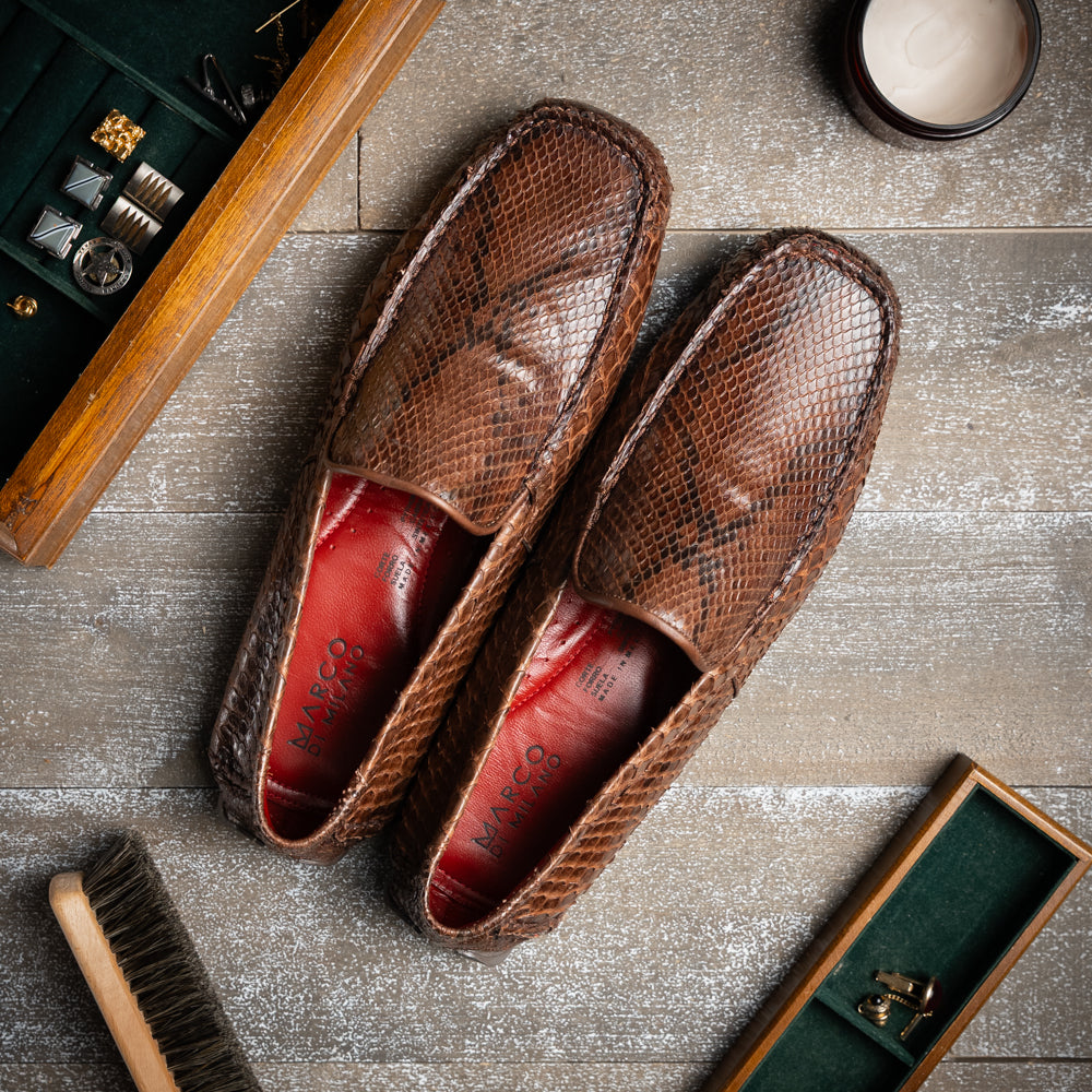A pair of Capri Brown luxury exotic shoes by Marco Di Milano, crafted from genuine python leather, with one handcrafted men’s loafer standing upright and the other displayed on its side to highlight the intricately textured sole.