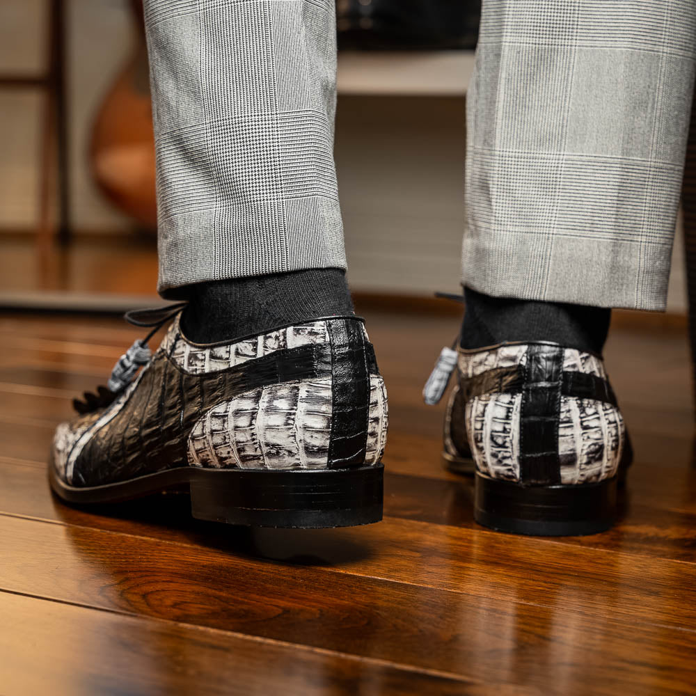 The Marco Di Milano Caribe Black / Newspaper are luxury men's derby shoes crafted from genuine hornback caiman crocodile leather in black and white, featuring red lining, leather soles, lace-up closures, and decorative tassels.