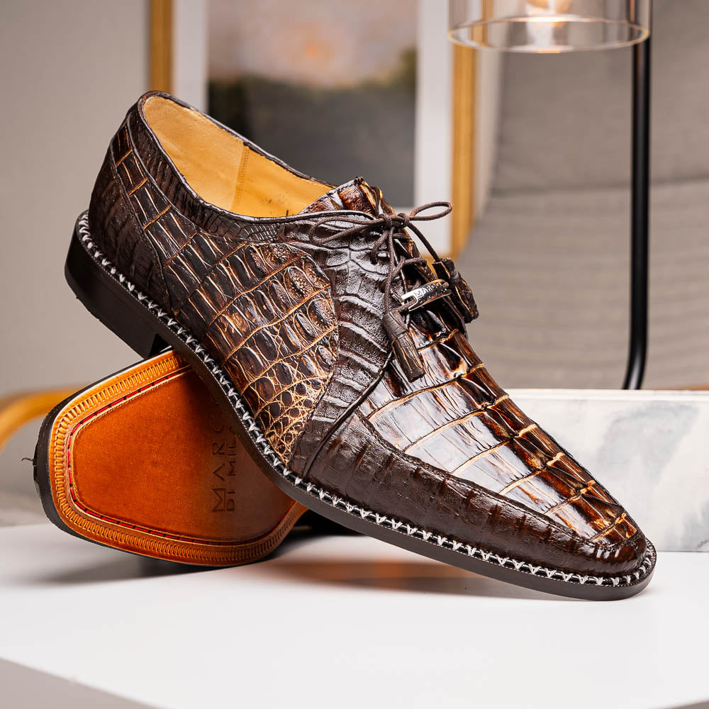 The Marco Di Milano Caribe Rustic Orix/Brown features luxury derby shoes crafted from genuine hornback caiman crocodile leather, with one upright and the other on its side showcasing a tan sole, visible stitching, and hand-painted finishes.