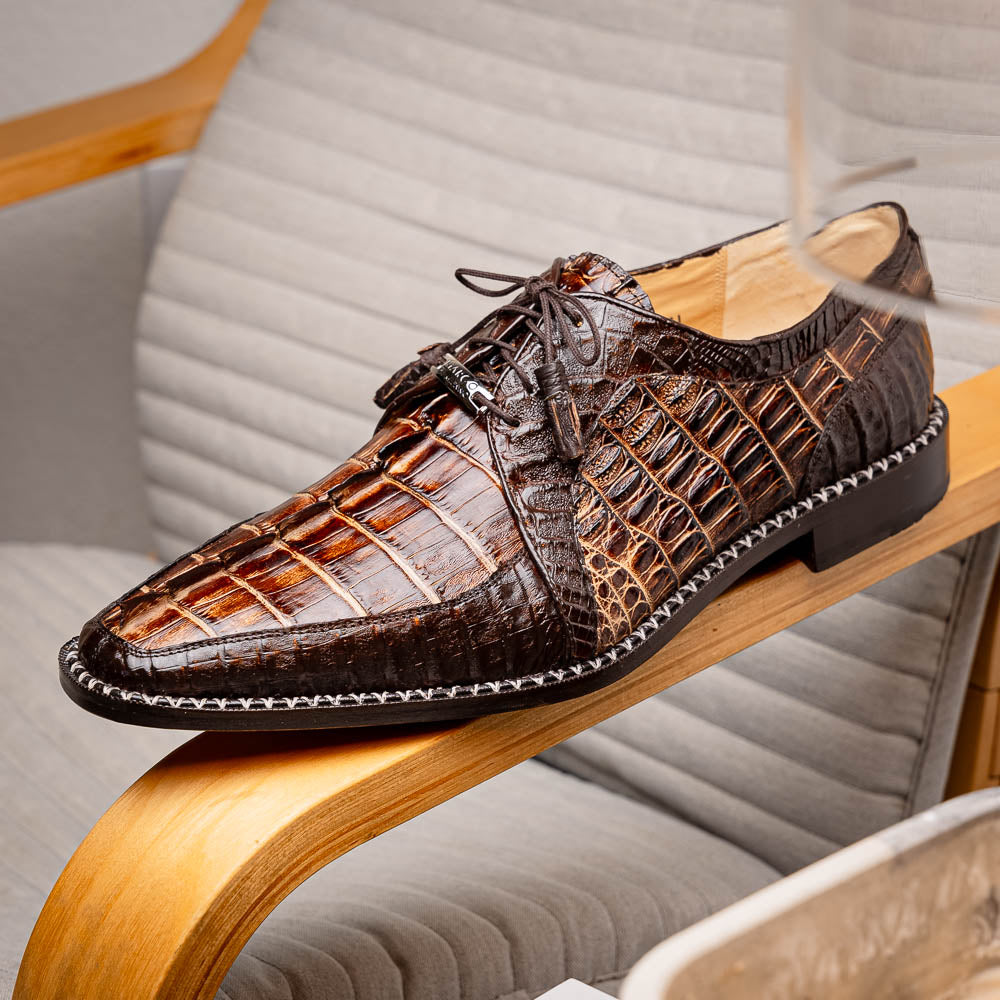 The Marco Di Milano Caribe Rustic Orix/Brown features luxury derby shoes crafted from genuine hornback caiman crocodile leather, with one upright and the other on its side showcasing a tan sole, visible stitching, and hand-painted finishes.