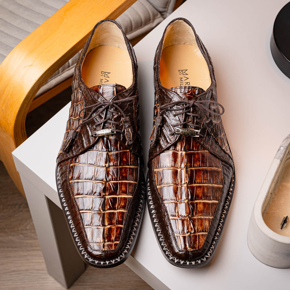 The Marco Di Milano Caribe Rustic Orix/Brown features luxury derby shoes crafted from genuine hornback caiman crocodile leather, with one upright and the other on its side showcasing a tan sole, visible stitching, and hand-painted finishes.