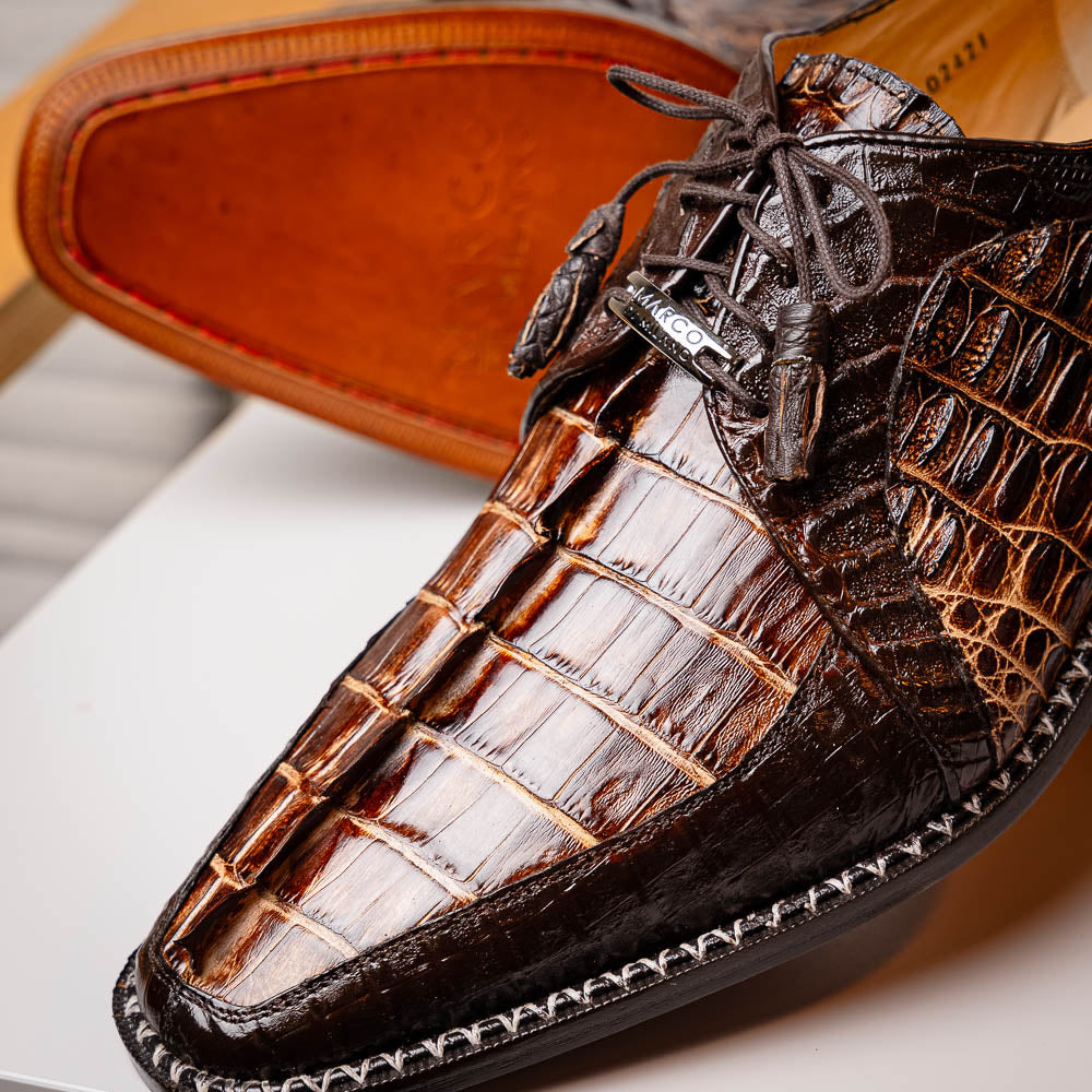 The Marco Di Milano Caribe Rustic Orix/Brown features luxury derby shoes crafted from genuine hornback caiman crocodile leather, with one upright and the other on its side showcasing a tan sole, visible stitching, and hand-painted finishes.