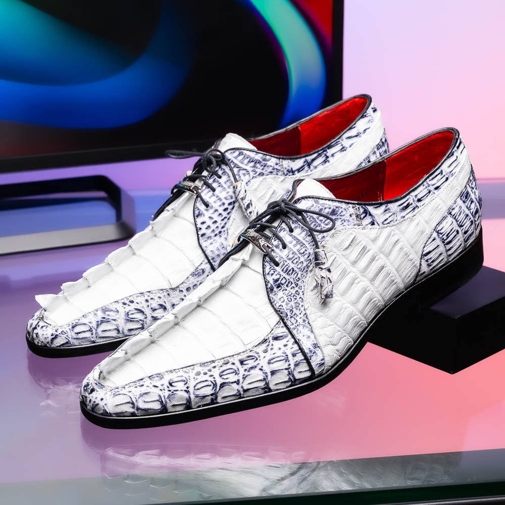The Marco Di Milano Caribe White / Newspaper Derby shoes feature white and black crocodile-patterned leather, one upright and one on its side to showcase a brown leather sole with red stitching—distinctive, exotic hand-painted footwear.