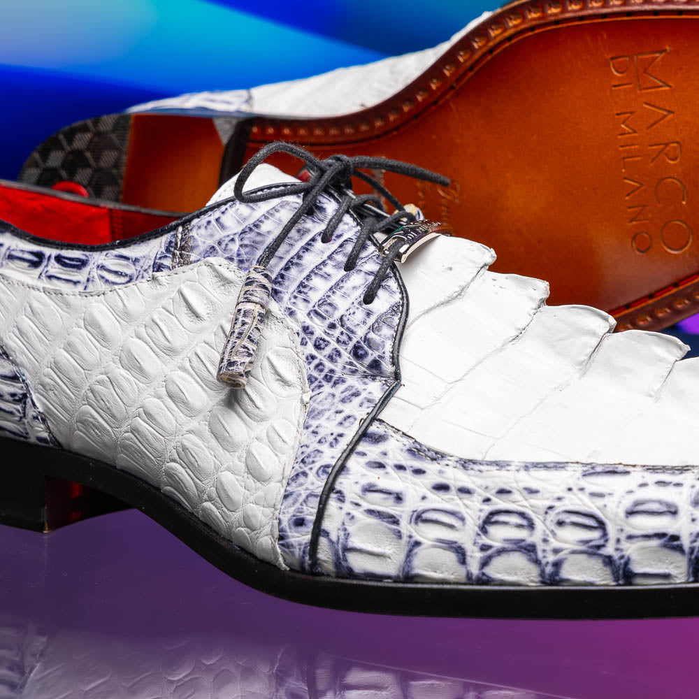 The Marco Di Milano Caribe White / Newspaper Derby shoes feature white and black crocodile-patterned leather, one upright and one on its side to showcase a brown leather sole with red stitching—distinctive, exotic hand-painted footwear.