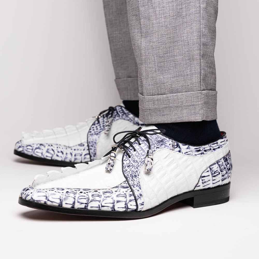 The Marco Di Milano Caribe White / Newspaper Derby shoes feature white and black crocodile-patterned leather, one upright and one on its side to showcase a brown leather sole with red stitching—distinctive, exotic hand-painted footwear.