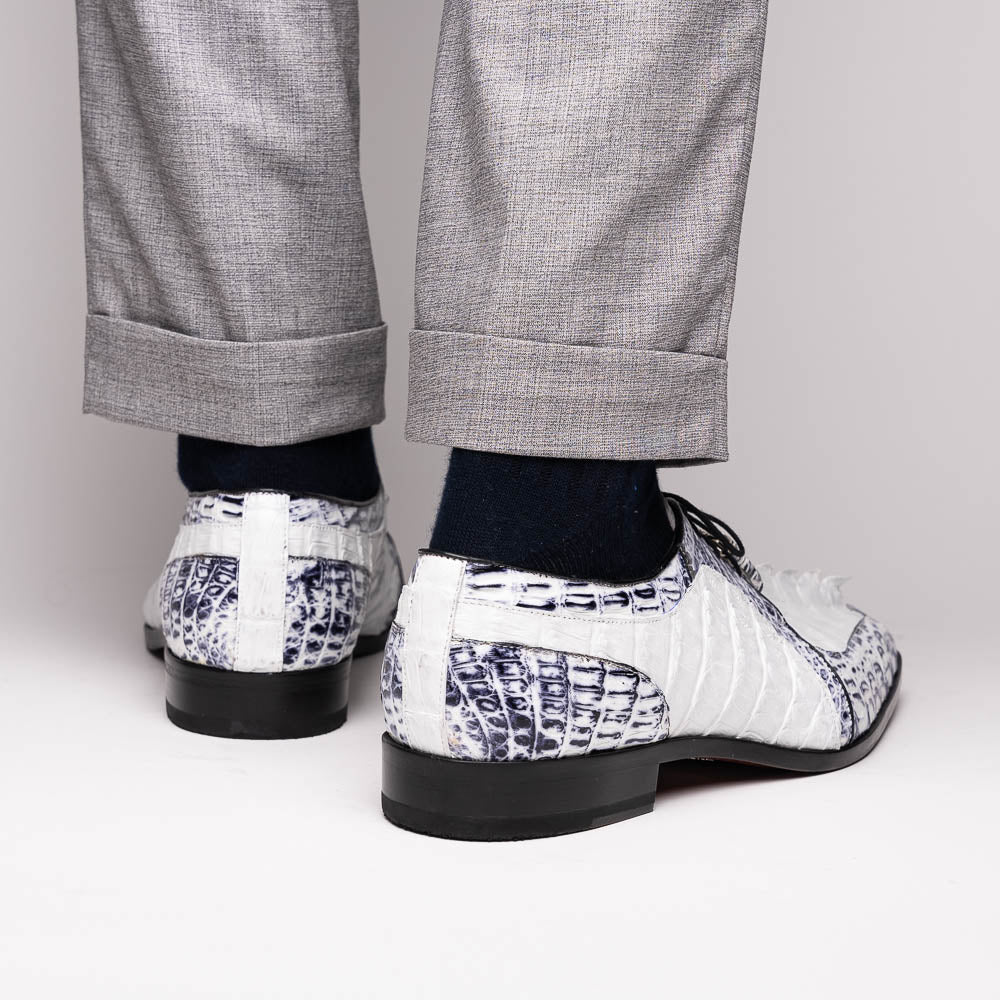 The Marco Di Milano Caribe White / Newspaper Derby shoes feature white and black crocodile-patterned leather, one upright and one on its side to showcase a brown leather sole with red stitching—distinctive, exotic hand-painted footwear.