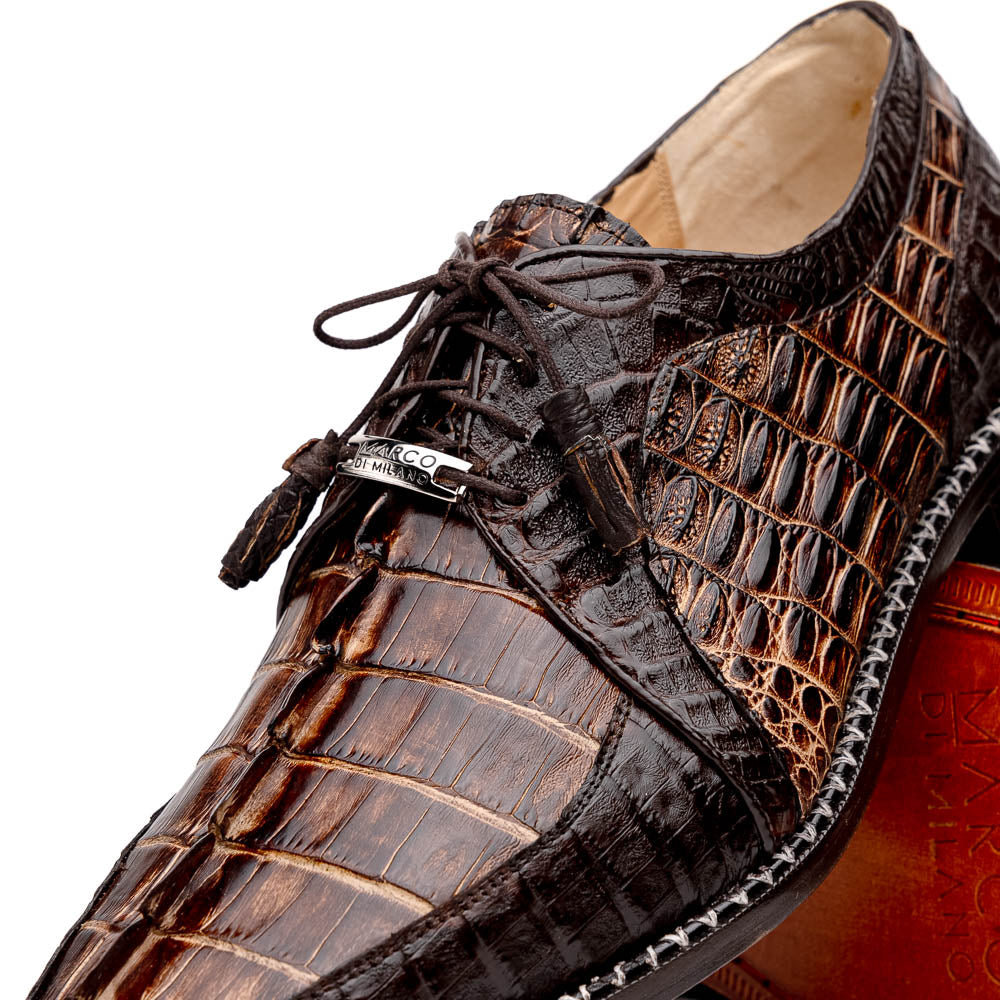 The Marco Di Milano Caribe Rustic Orix/Brown features luxury derby shoes crafted from genuine hornback caiman crocodile leather, with one upright and the other on its side showcasing a tan sole, visible stitching, and hand-painted finishes.