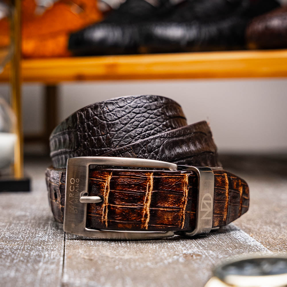 The Marco Di Milano Caribe Belt Brown / Pantano, a luxurious men's belt crafted from exotic caiman fuscus leather in brown and black with a silver buckle, is coiled against a white background.