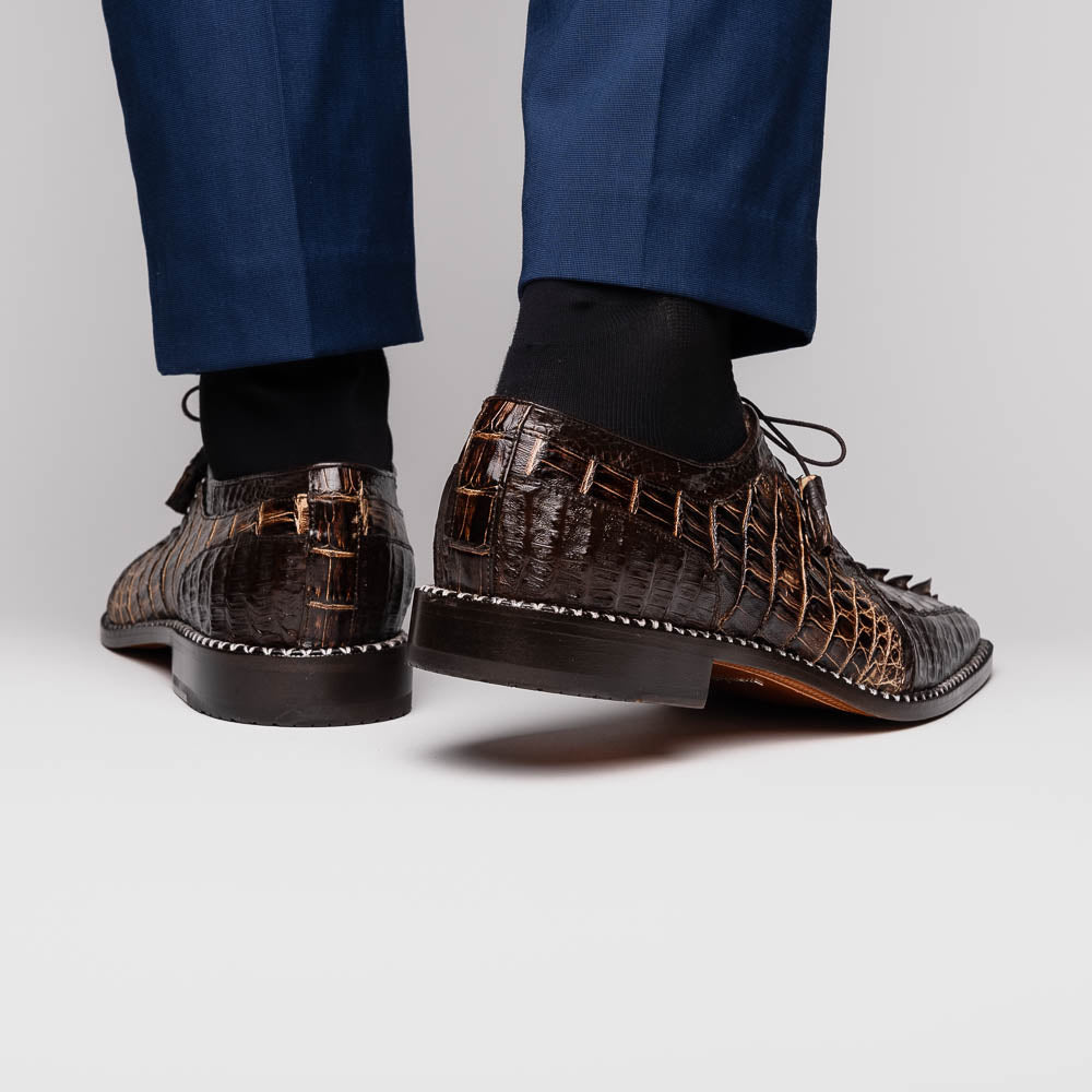 The Marco Di Milano Caribe Rustic Orix/Brown features luxury derby shoes crafted from genuine hornback caiman crocodile leather, with one upright and the other on its side showcasing a tan sole, visible stitching, and hand-painted finishes.
