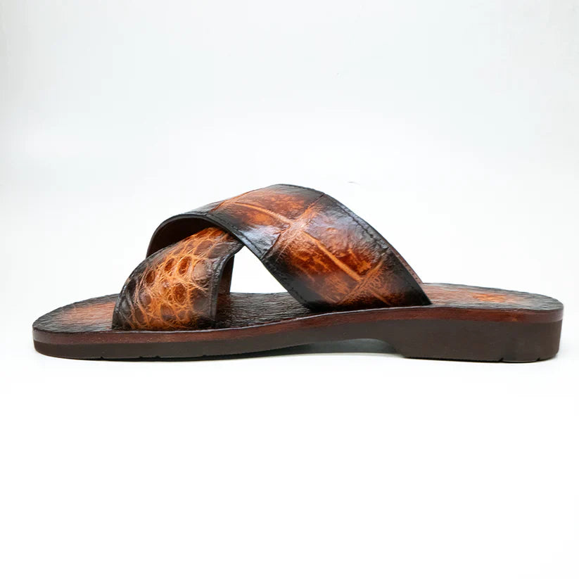 The Elios Honey by Marco Di Milano is a luxury brown leather sandal with a crocodile-textured finish and two crisscross straps, hand painted for elegance and showcased on a white background.