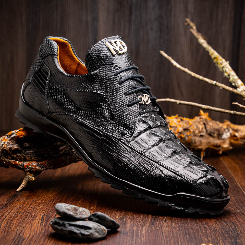 The Crater Black by Marco Di Milano features black textured leather with a crocodile pattern and metallic logo accents, exemplifying genuine exotic shoe craftsmanship—one shoe stands upright, the other lies on its side.