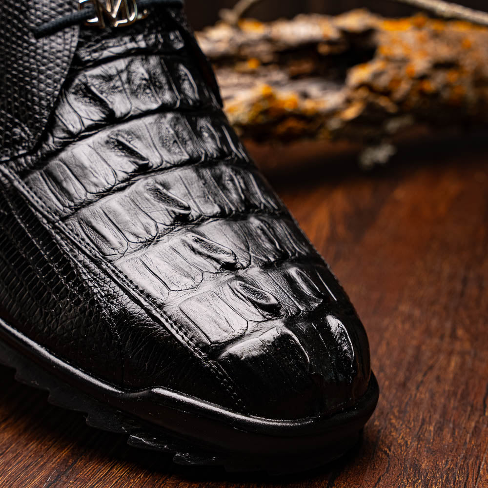 The Crater Black by Marco Di Milano features black textured leather with a crocodile pattern and metallic logo accents, exemplifying genuine exotic shoe craftsmanship—one shoe stands upright, the other lies on its side.