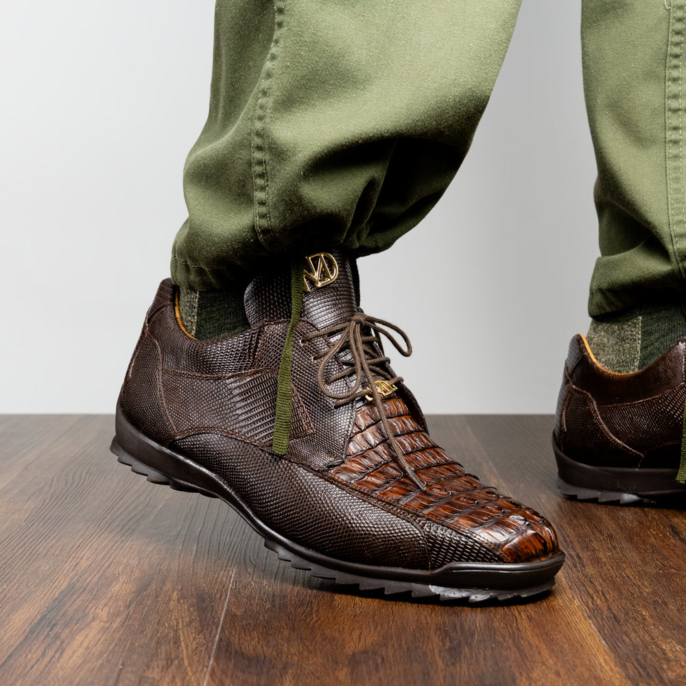 The Crater Brown by Marco Di Milano features brown textured leather with crocodile pattern accents, gold "MD" logos, and black rubber soles, blending dress shoe elegance with caiman hornback sneaker style.