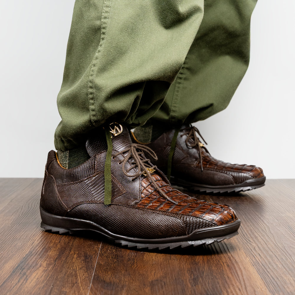 The Crater Brown by Marco Di Milano features brown textured leather with crocodile pattern accents, gold "MD" logos, and black rubber soles, blending dress shoe elegance with caiman hornback sneaker style.