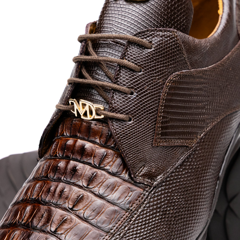 The Crater Brown by Marco Di Milano features brown textured leather with crocodile pattern accents, gold "MD" logos, and black rubber soles, blending dress shoe elegance with caiman hornback sneaker style.