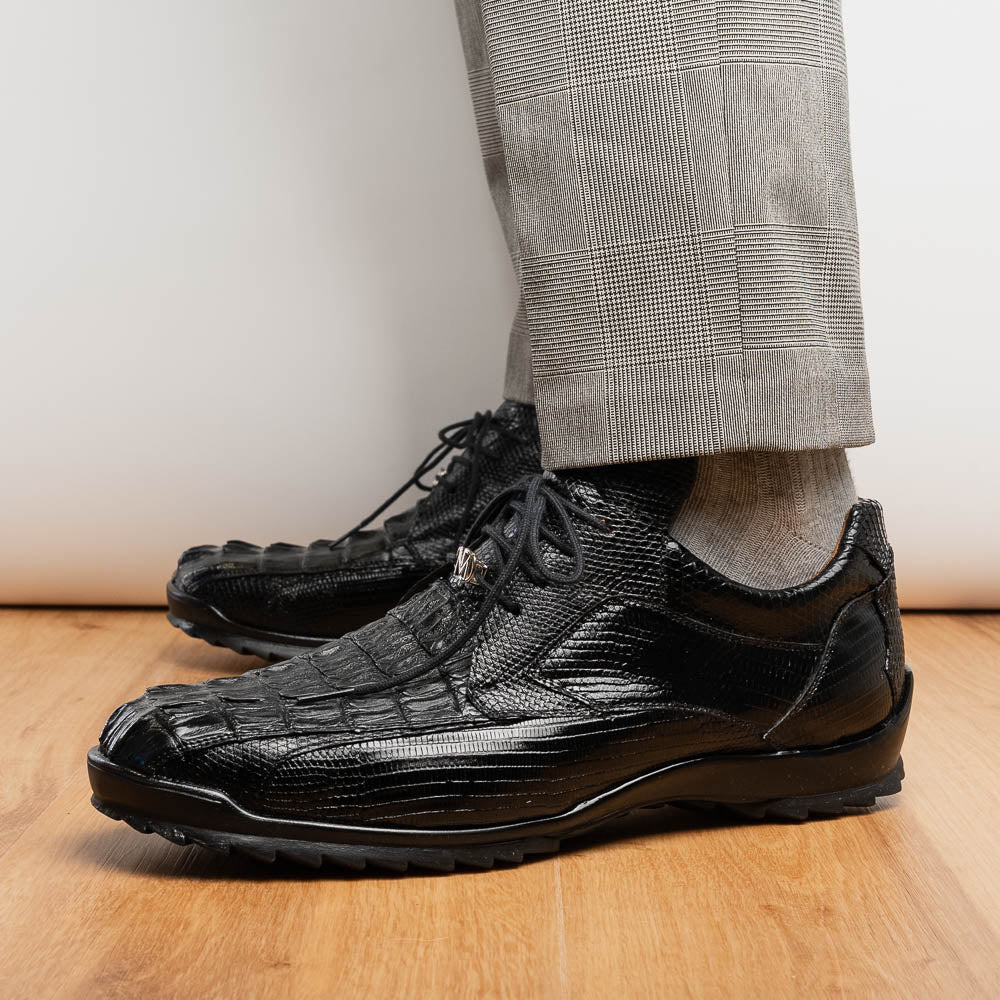 The Crater Black by Marco Di Milano features black textured leather with a crocodile pattern and metallic logo accents, exemplifying genuine exotic shoe craftsmanship—one shoe stands upright, the other lies on its side.