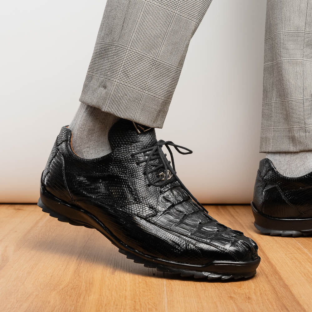 The Crater Black by Marco Di Milano features black textured leather with a crocodile pattern and metallic logo accents, exemplifying genuine exotic shoe craftsmanship—one shoe stands upright, the other lies on its side.