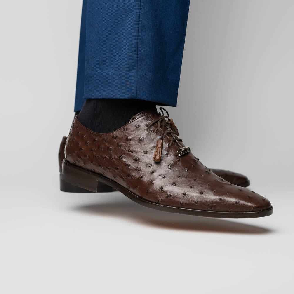 The Criss Brown by Marco Di Milano is a pair of luxury dress oxfords in dark brown genuine ostrich quill leather with decorative laces and a leather sole, shown with one shoe elegantly displayed on its side atop the other.