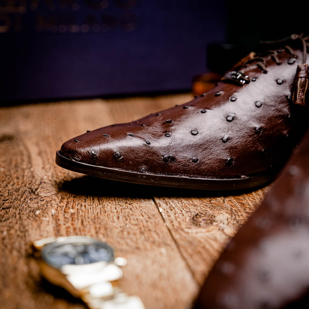 The Criss Brown by Marco Di Milano is a pair of luxury dress oxfords in dark brown genuine ostrich quill leather with decorative laces and a leather sole, shown with one shoe elegantly displayed on its side atop the other.