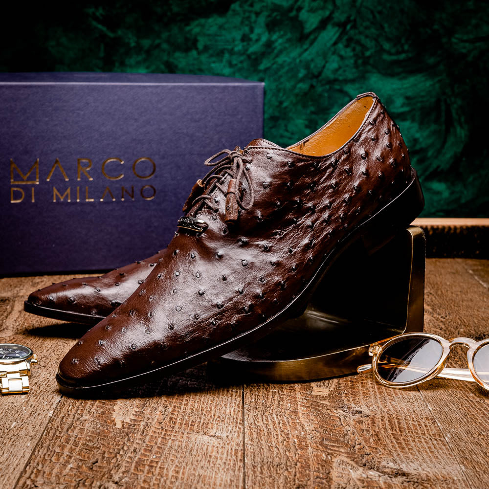 The Criss Brown by Marco Di Milano is a pair of luxury dress oxfords in dark brown genuine ostrich quill leather with decorative laces and a leather sole, shown with one shoe elegantly displayed on its side atop the other.