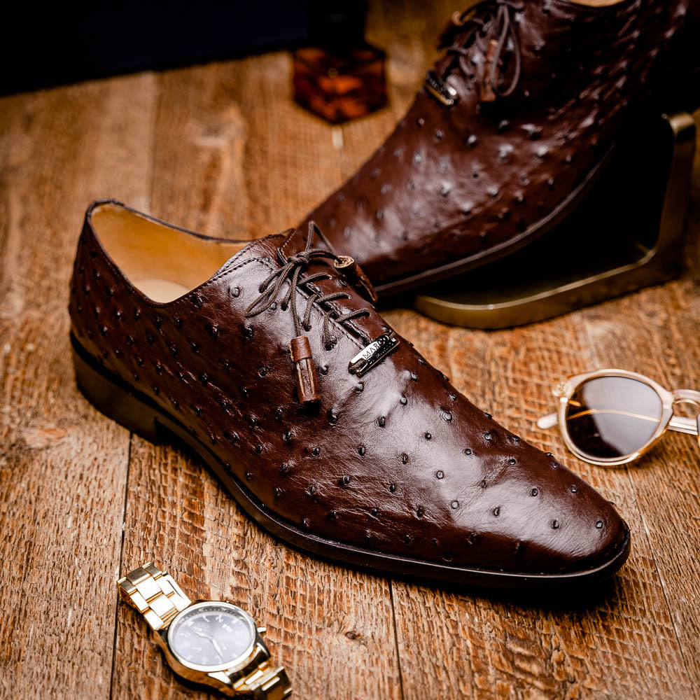 The Criss Brown by Marco Di Milano is a pair of luxury dress oxfords in dark brown genuine ostrich quill leather with decorative laces and a leather sole, shown with one shoe elegantly displayed on its side atop the other.