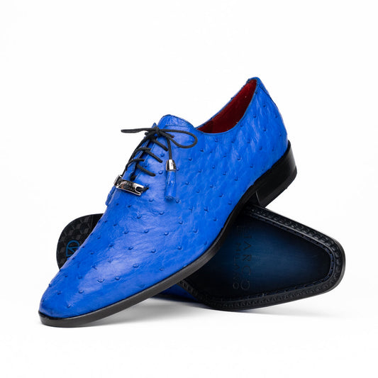 Introducing the Criss Electric Blue by Marco Di Milano—a pair of vibrant blue genuine ostrich quill leather oxford dress shoes featuring stylish laces and sleek metal detailing. One shoe stands upright while the other displays its beautifully crafted sole, making them an exceptional choice for anyone looking for distinctive luxury footwear.