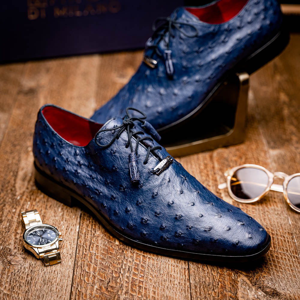 The Criss Navy by Marco Di Milano: a pair of genuine ostrich dress shoes with blue leather, black laces, red inner lining, and brown soles—one upright, one on its side—showcasing luxury men’s footwear.