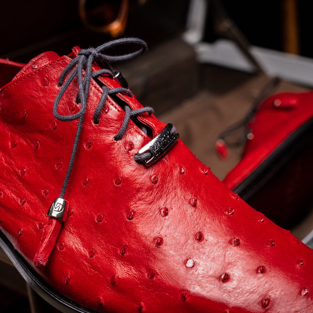 Introducing the Criss Red by Marco Di Milano: a pair of striking red genuine ostrich quill leather dress oxford shoes with black laces—one elegantly upright and the other displayed on its side to showcase the luxurious sole. This luxury footwear commands attention at every step.
