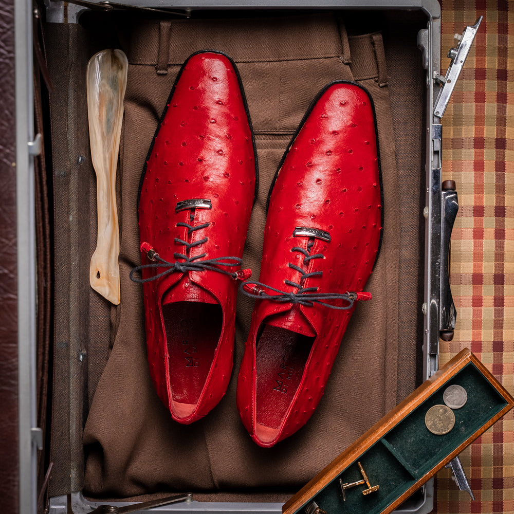 Introducing the Criss Red by Marco Di Milano: a pair of striking red genuine ostrich quill leather dress oxford shoes with black laces—one elegantly upright and the other displayed on its side to showcase the luxurious sole. This luxury footwear commands attention at every step.