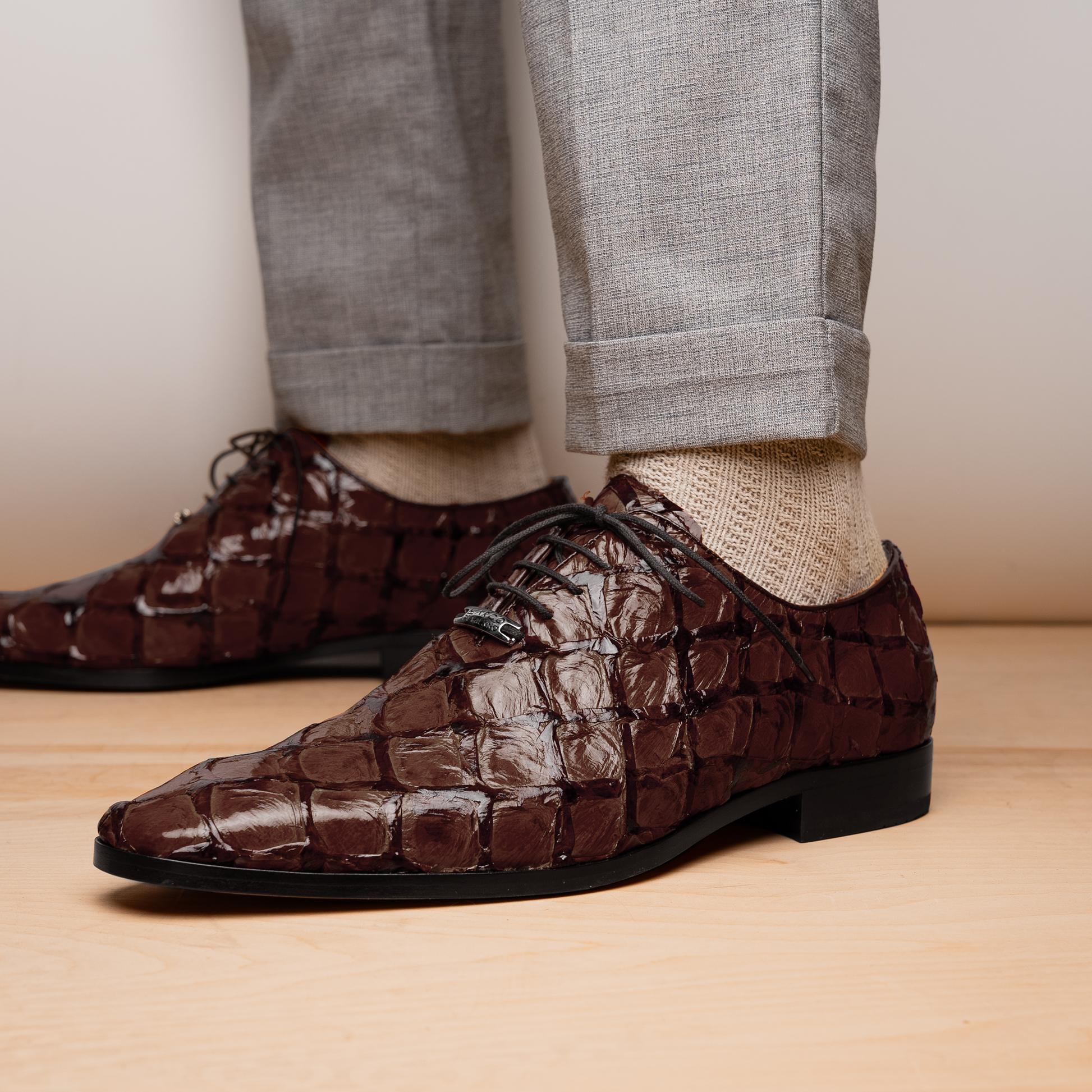 A pair of Olivieri Brown oxford shoes by Marco Di Milano—one upright, one on its side revealing the branded sole—showcase luxurious crocodile leather craftsmanship.