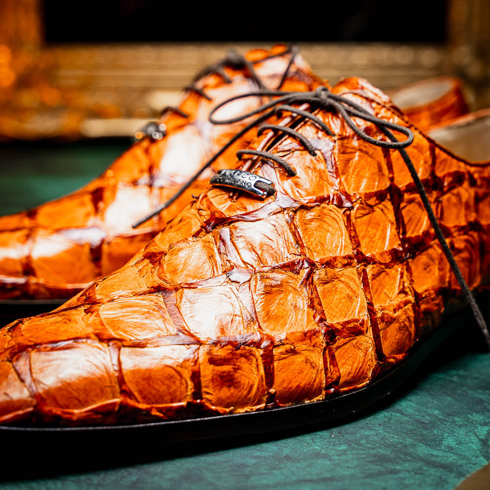 A pair of Olivieri Brandy by Marco Di Milano luxury dress oxford shoes in orange-brown crocodile leather with dark laces, one shoe shown on its side highlighting the branded sole.