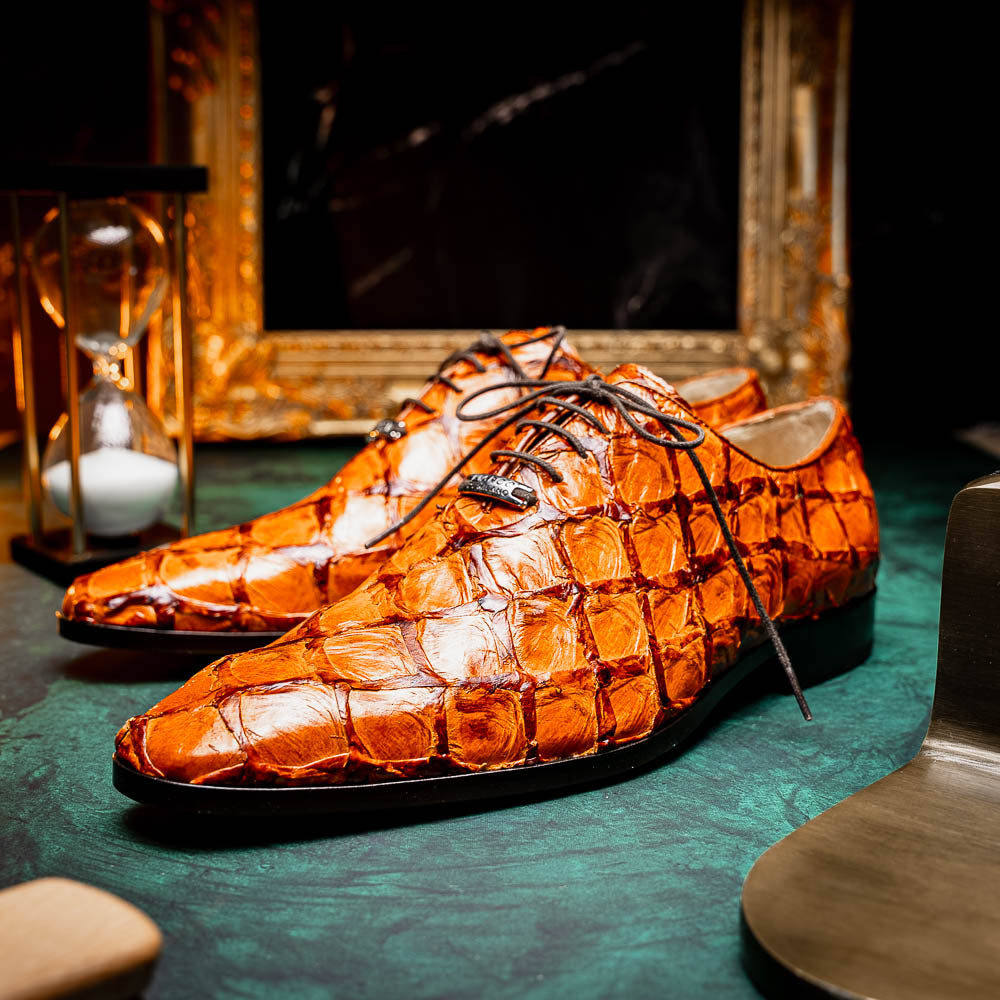 A pair of Olivieri Brandy by Marco Di Milano luxury dress oxford shoes in orange-brown crocodile leather with dark laces, one shoe shown on its side highlighting the branded sole.