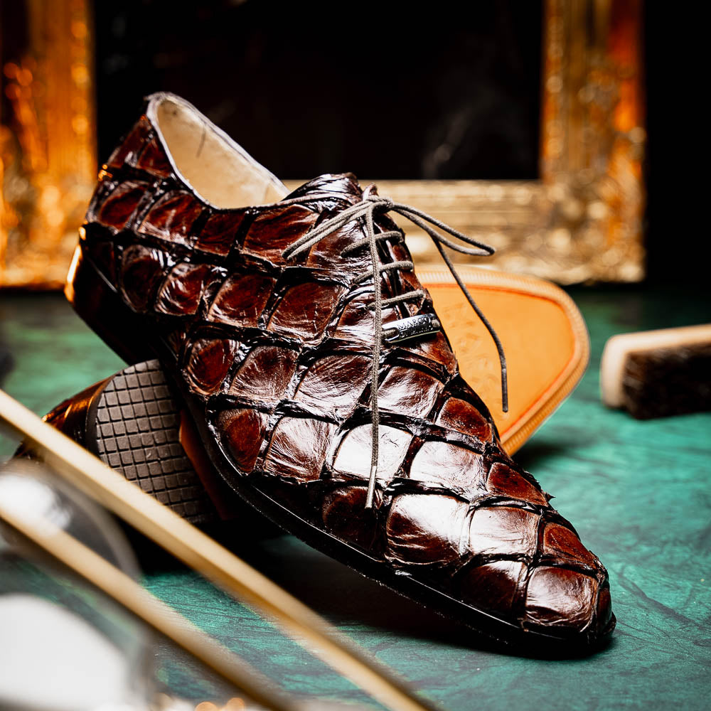 A pair of Olivieri Brown oxford shoes by Marco Di Milano—one upright, one on its side revealing the branded sole—showcase luxurious crocodile leather craftsmanship.