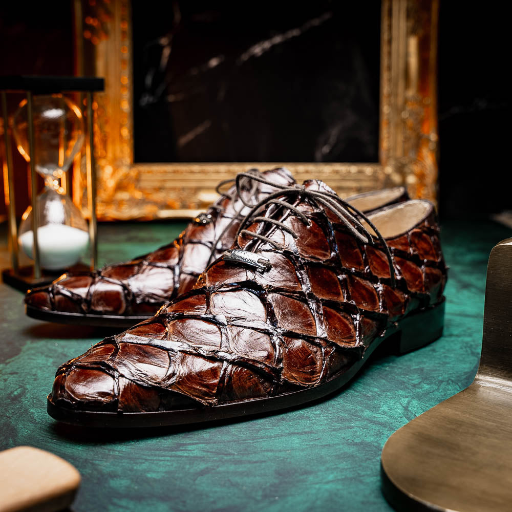 A pair of Olivieri Brown oxford shoes by Marco Di Milano—one upright, one on its side revealing the branded sole—showcase luxurious crocodile leather craftsmanship.