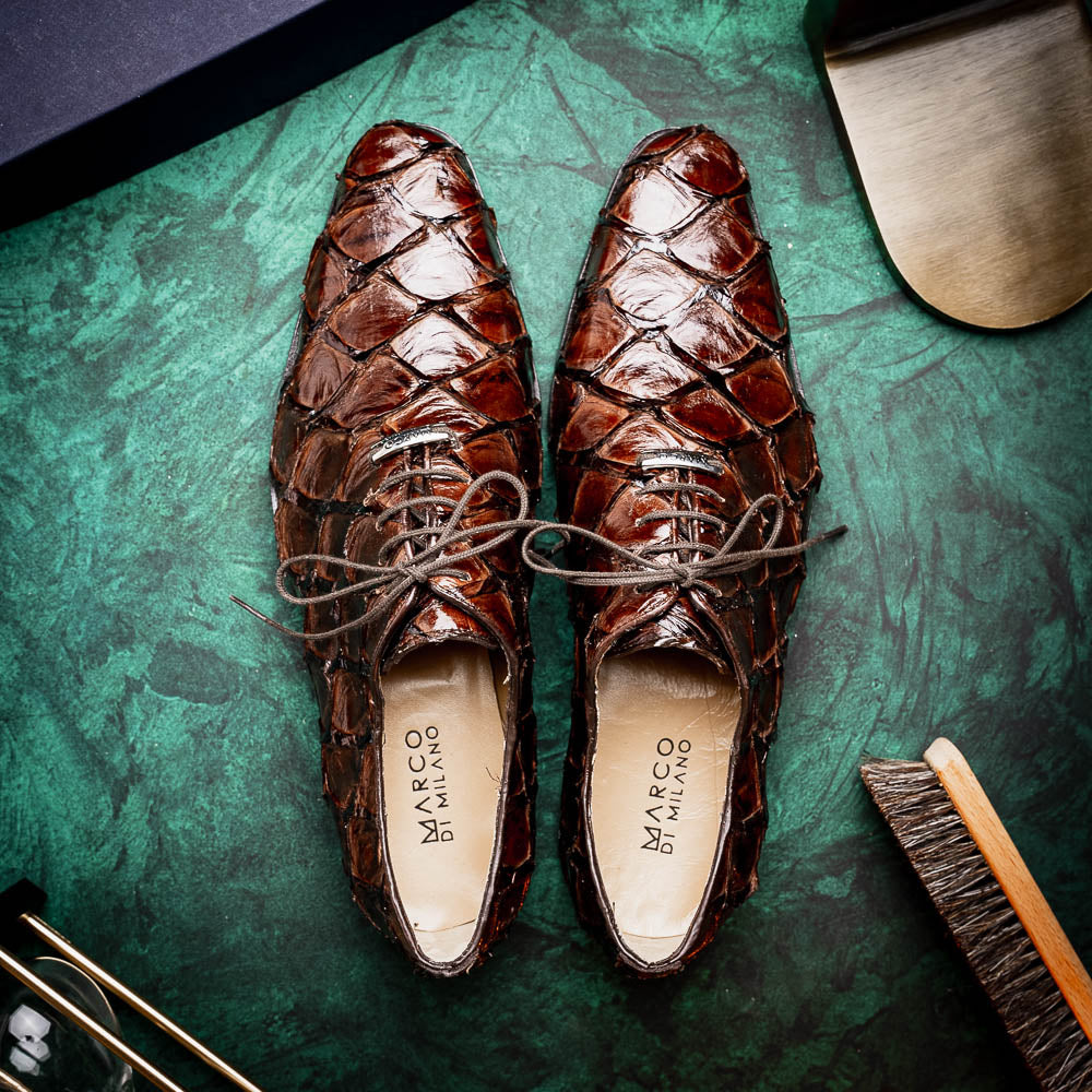 A pair of Olivieri Brown oxford shoes by Marco Di Milano—one upright, one on its side revealing the branded sole—showcase luxurious crocodile leather craftsmanship.