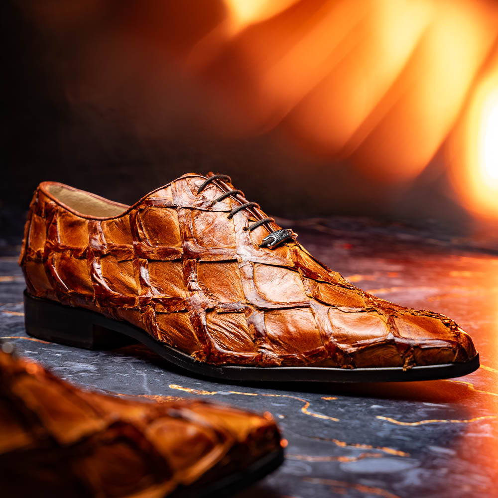 A pair of Olivieri Cognac dress shoes by Marco Di Milano, crafted from brown crocodile leather with black laces—one shoe stands upright, the other shows its sole—ideal for lovers of luxury footwear.