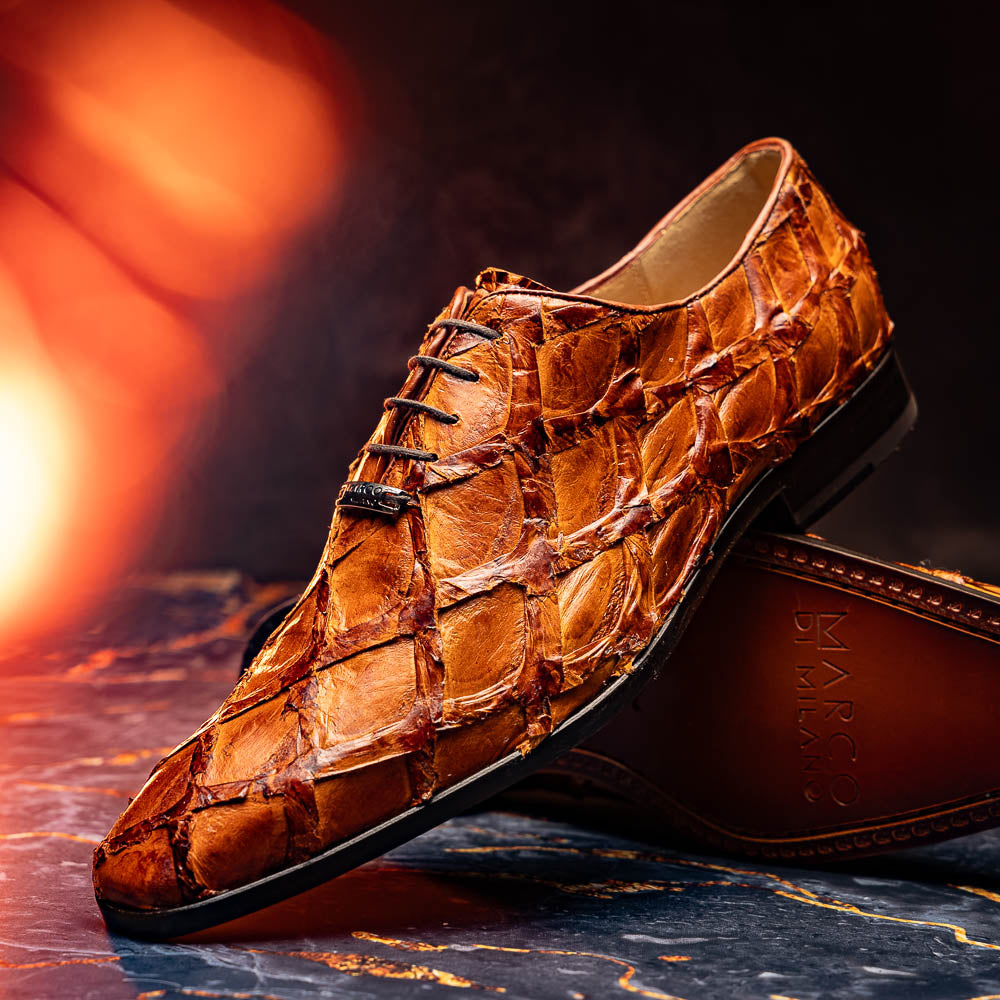 A pair of Olivieri Cognac dress shoes by Marco Di Milano, crafted from brown crocodile leather with black laces—one shoe stands upright, the other shows its sole—ideal for lovers of luxury footwear.