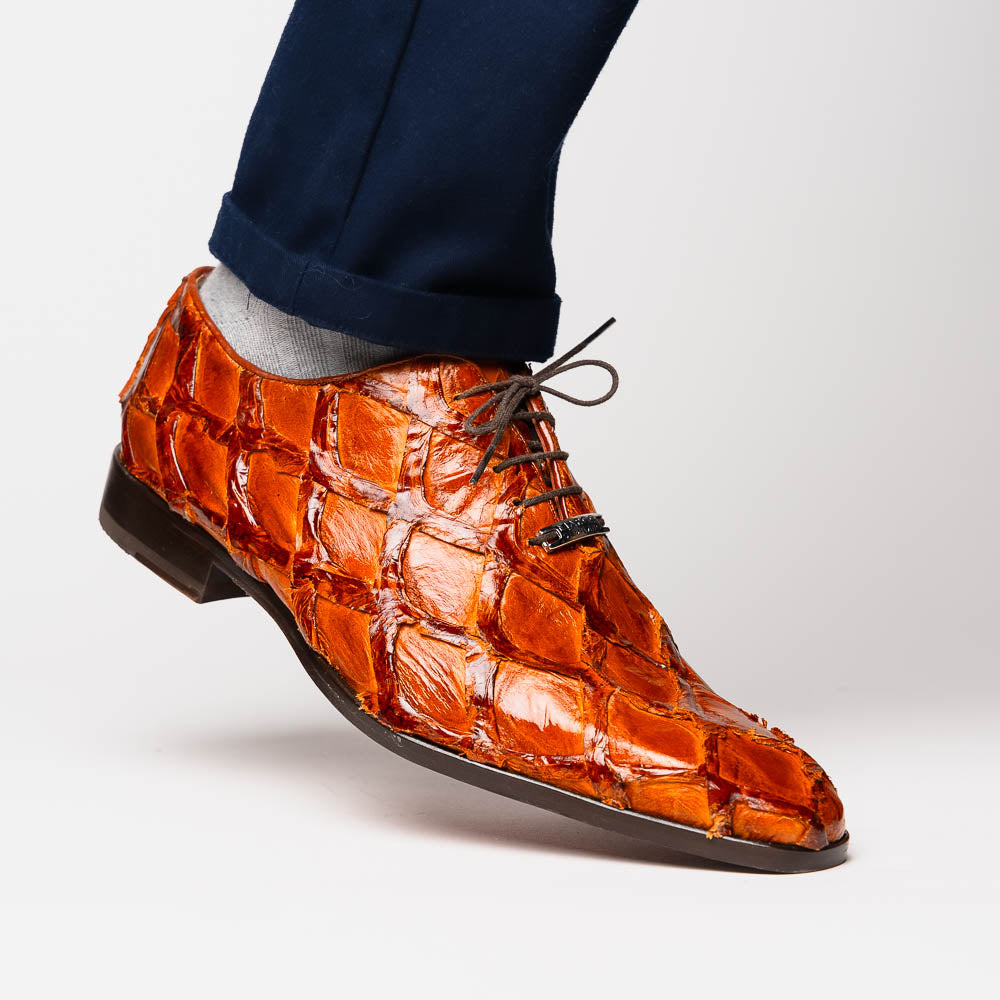 A pair of Olivieri Cognac dress shoes by Marco Di Milano, crafted from brown crocodile leather with black laces—one shoe stands upright, the other shows its sole—ideal for lovers of luxury footwear.