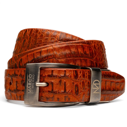 The Riccardo Belt Brandy by Marco Di Milano is a brown exotic leather belt with a crocodile pattern, silver buckle engraved with "Marco Di Milano" and "MD," styled after caiman fuscus-belly belts for a refined look.