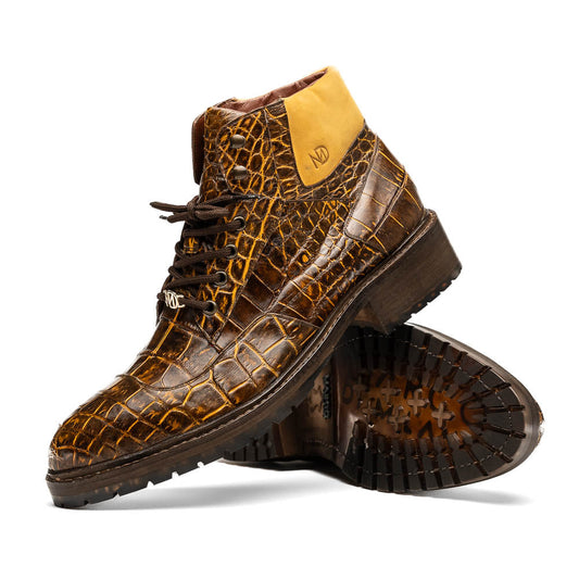 The Potenza Mustard/Brown boots by Marco Di Milano feature brown crocodile-pattern leather, lace-up fronts, tan ankle detail, and textured rubber soles with hand-painted finishes—one boot upright, the other on its side.