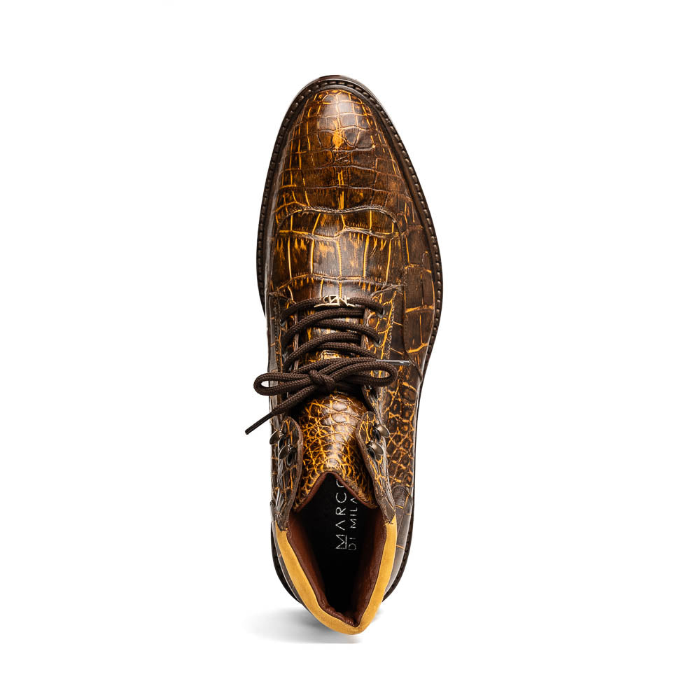 The Potenza Mustard/Brown boots by Marco Di Milano feature brown crocodile-pattern leather, lace-up fronts, tan ankle detail, and textured rubber soles with hand-painted finishes—one boot upright, the other on its side.